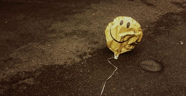 Deflated smiley balloon on a wet road symbolizing resilience, positive mindset, and the psychology of good vibes during difficult times.